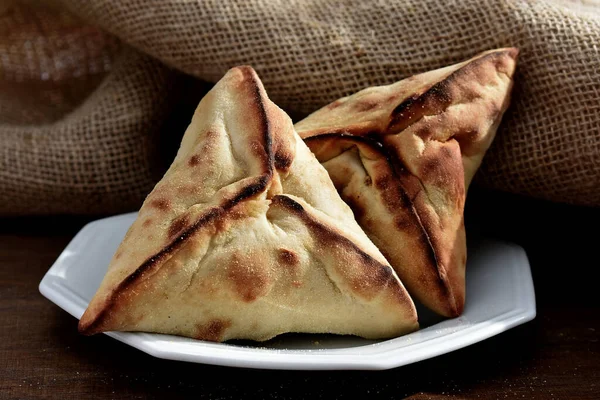 Beyaz bir tabakta et ve soğanla doldurulmuş Arap Pastası ve arka planda kırsal kumaş.