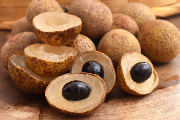 Bir demet altın litchi ya da ahşap bir masada ejderha gözü meyvesi ve arka planda bir hasır sepet.
