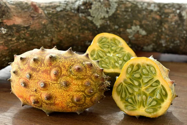 The Kiwano or horned melon african fruit on wooden table and a tree branch at background