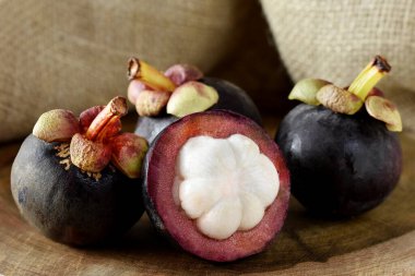 Ahşap bir masada Asyalı Mangosteen meyvesi ve arka planda kırsal kumaş.