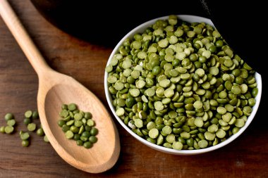 Masanın üzerinde tahta kaşıkta yeşil bezelyeler.