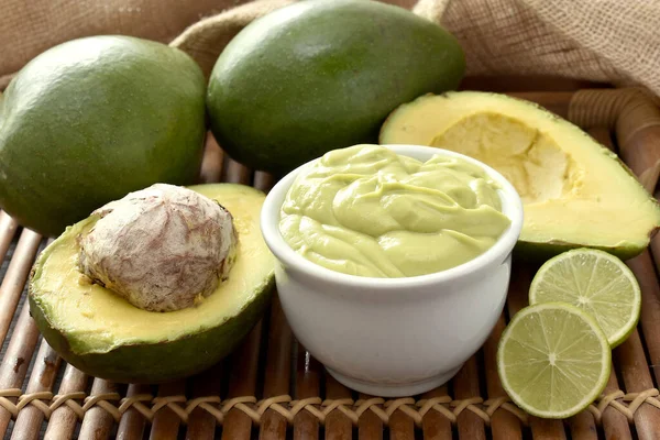 Kâsede avokado kremalı meyve ve bambu tepsisinde limon dilimleri ve arka planda kırsal kumaş.