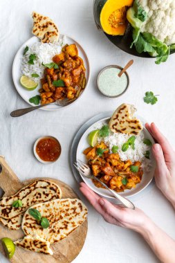Vejetaryen Hint köri soslu, karnabahar ve balkabaklı raita, naan ekmeği ve mango turşusuyla servis edilen beyaz arka planda Basmati pilavı, kadın eli tek tabak.