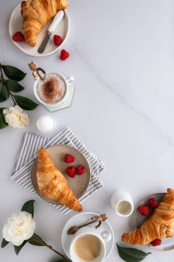 Kahvaltı masasında ayçöreği, kahve, ahududu, kan portakalı, kaynamış yumurta ve çiçekler beyaz ahşap bir masa üzerinde beyaz mermer bir yüzey üzerinde.