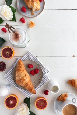 Üzerinde reçel, kahve, ahududu, kan portakalı, kaynamış yumurta ve çiçekler olan bir kahvaltı masası.