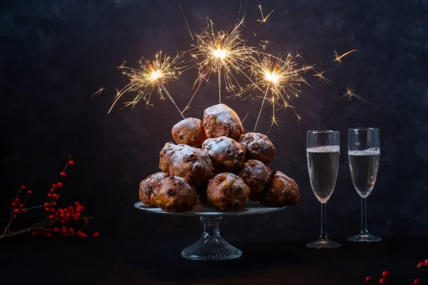 Bir yığın oliebollen (çeviri: Hollanda hamur ateşleyicisi) yatay çekim siyah arka planda üç maytap ve iki bardak şampanya ile