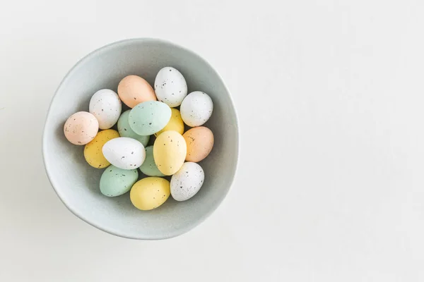 Çikolatalı paskalya yumurtası pastel renklerde soldaki mavi kasede beyaz arka planda, düz bir şekilde fotokopi alanı ile yatıyordu.
