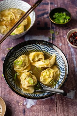 İki kâse ev yapımı sebze wonton çorbası, tofu ve brokoli ile ahşap masada servis edilen, kırmızı biber yağı, sağlıklı beslenme, vejetaryen diyeti.