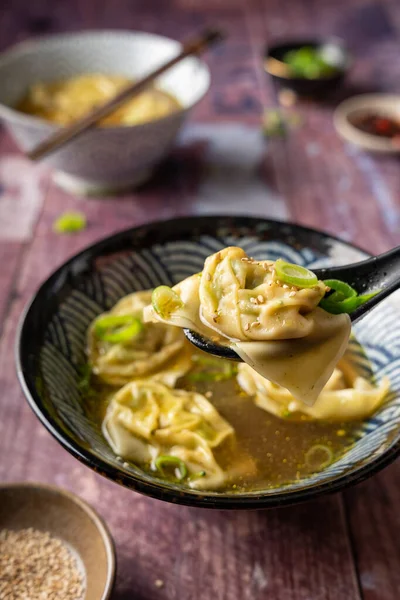 İki kâse ev yapımı sebze wonton çorbası tofu ve brokolili. Bir kaşık, ahşap masada servis edilen bir hamur köftesi. Yanında çubuklar ve kırmızı biber yağı, sağlıklı beslenme, vejetaryen diyeti.