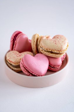 Pembe yuvarlak bir tabakta, vanilya ve çilek aromalı kalp şeklinde Fransız kurabiyeleri, tarafsız arka planda kopyalama alanı, dikey