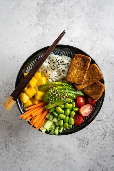 Tofu, mango, avokado, havuç, edamame, domates, salatalık ve gri arka planda dikey salatalıklı ev yapımı vejetaryen dürüm kasesi.