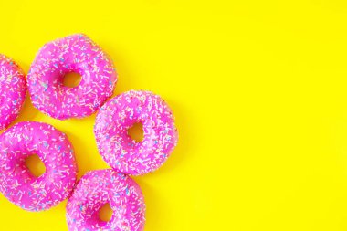 Sarı arka plan manzaralı pembe kremalı çörekler. Mesaj için yer. Şeker, abur cubur, hamur işi. Parlak renkler