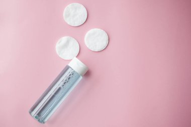 Pamuk pedler, tonik ya da mikiler ile temizleyici su, taze otlar ve pembe arka planda çiçekler, üst manzara. Güzellik, cilt, saç veya vücut bakımı kavramı. Seçici odak.