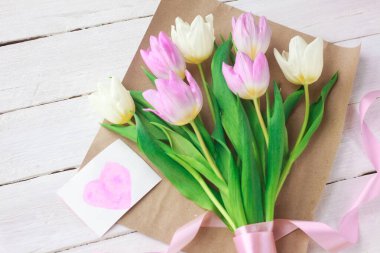 Kadınlar Günü. Beyaz ahşap arka planda bir buket lale ve içinde kalpler olan bir kart. seçici odak.