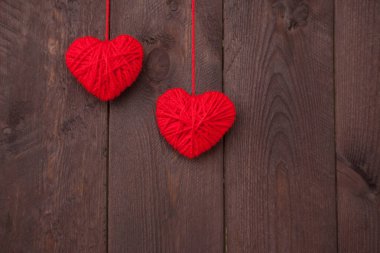 Ahşap arka planda kırmızı yün iplikten yapılmış iki kalp. Sevgililer Günü konsepti.