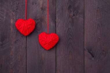 Ahşap arka planda kırmızı yün iplikten yapılmış iki kalp. Sevgililer Günü konsepti.