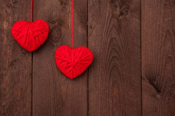 Ahşap arka planda kırmızı yün iplikten yapılmış iki kalp. Sevgililer Günü konsepti.