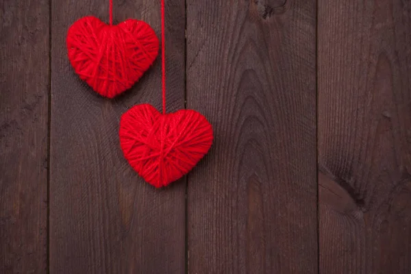 Ahşap arka planda kırmızı yün iplikten yapılmış iki kalp. Sevgililer Günü konsepti.