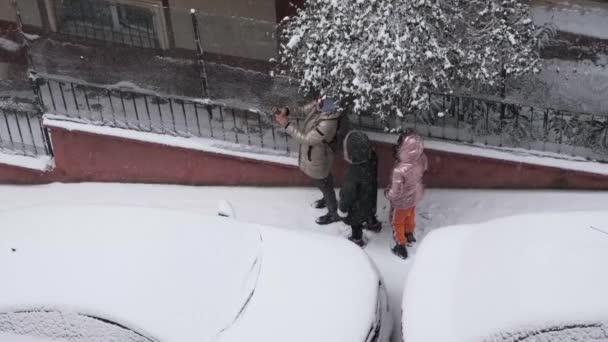 Seorang ibu yang tidak dikenal mengambil selfie dengan anak-anak bermain di salju pada waktu musim dingin dari sudut yang tinggi — Stok Video