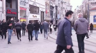 Beyoğlu, İstanbul, Türkiye - 02.17.2021: Taksim 'deki İstiklal Caddesi' nin başlangıç noktası ve maskeli kişilerin yürüdüğü caddenin girişindeki tramvay yolu uzak ihtimal.