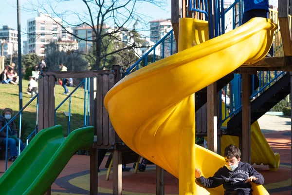 Kadıköy, İstanbul, Türkiye - 02.18.2021: Covid maskeli bir çocuk kaydırak kayarken, aileler Özgürlük Parkı 'nda bekliyor