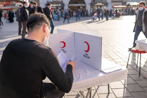 Eminonu, İstanbul, Türkiye - 02.26.2021: bir erkek kan bağışı gönüllüsü, kan dökme operasyonundan önce oturup Türk Kızılayı 'nın (Türk Kızılhaç) izin formunu okuyor