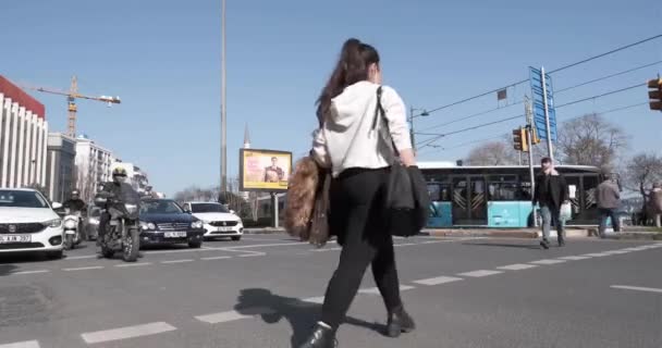 Beyoglu, Estambul, Turquía - 03.17.2021: una mujer y algunos peatones cruzan la carretera con luz verde y los coches y motocicletas se detienen en la ciudad de Findikli a la luz del día — Vídeos de Stock