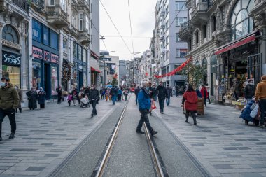 Beyoğlu, İstanbul, Türkiye - 03.12.2021: Taksim 'deki Istiklal Caddesi' nde koruyucu maskeli bir çok insan yürüyor ve sokakta fotokopi alanı ile tramvay yolu var