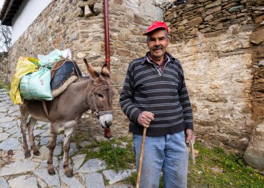Sirince, İzmir, Türkiye - 03.08.2021: Türk köylü ve köylünün yerel giyimi ve eyer gülüşlü eşek ve İlkbaharda Sirince köyündeki kameraya bakın