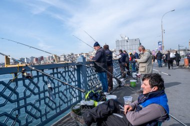 Eminonu, İstanbul, Türkiye - 04.13.2021: portatif sandalyede oturan ve Galata Köprüsü yakınlarında demir balıkçı oltası kullanan ve temiz havada balık bekleyen bir adam
