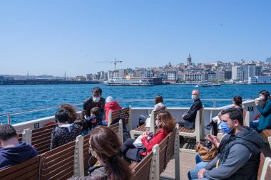 İstanbul, Türkiye - 04.29.2021: koltuklarda oturan ve deniz, Galata Köprüsü ve Kule 'ye bakan bir grup koruyucu maskeli Türk gemi yolcusu