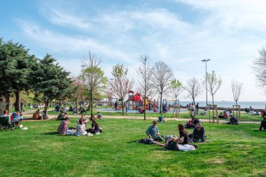 Kadıköy, İstanbul, Türkiye - 04.29.2021: Karantina gününden önce Moda Kamu Parkı ve açık bir bahar gününde bir çok insan yeşil çimlerin üzerinde fotokopi alanı ile oturup dinleniyor