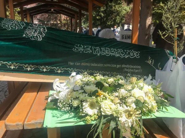 Sisli, İstanbul, Türkiye - 04.20.2021: Zincirlikuyu Mezarlığı ve İslam metnindeki yeşil örtülü ahşap Türk tabutu ve çiçekleri (çeviri: her ruh ölümü tadacak. Sonra bize döndürüleceksiniz.)