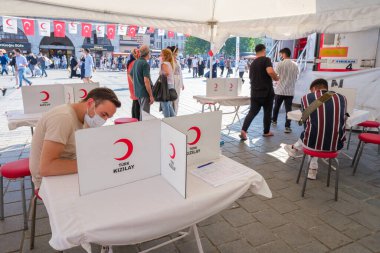 Eminonu, İstanbul, Türkiye - 07.05.2021: Türk Kızılayı (Türk Kizilay) logosu gönüllülerin kalabalık bir meydanda fotokopi alanı olan onay belgeleri imzaladığı beyaz masa üzerinde
