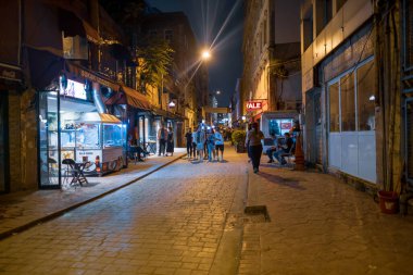Beyoğlu, İstanbul, Türkiye - 07.07.2021: Karaköy Caddesi ve gece saatlerinde parlak ışıkları olan küçük dükkanlar ve bazı insanlar gezici gezi gezisi kavramları için geziyorlar