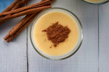 Beyaz ahşap bir masanın üzerinde tarçınlı ev yapımı vanilyalı krema. Süt, yumurta, vanilya ve tarçınlı lezzetli bir tatlı. en üstteki görünüm