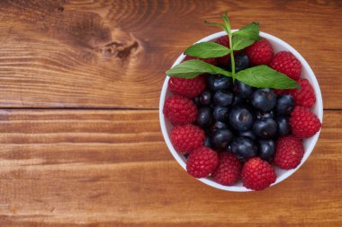 Böğürtlen ve ahududu beyaz bir kase içinde ahşap bir masanın üzerinde. Sağlıklı bir kahvaltı veya atıştırmalık için lezzetli bir fikir..