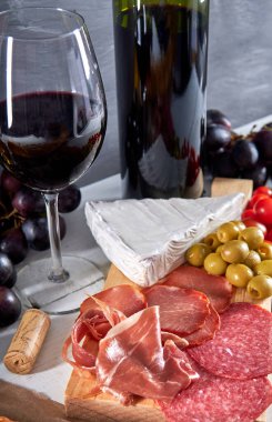 Et tabağı ve şarap. çeşitli jambonlar, zeytinler, domatesler, üzümler ve brie peyniri (Antipasto veya tapas). Herkesle paylaşmak için lezzetli bir seçim.