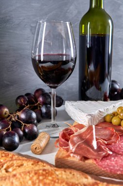 Et tabağı ve şarap. çeşitli jambonlar, zeytinler, domatesler, üzümler ve brie peyniri (Antipasto veya tapas). Herkesle paylaşmak için lezzetli bir seçim.