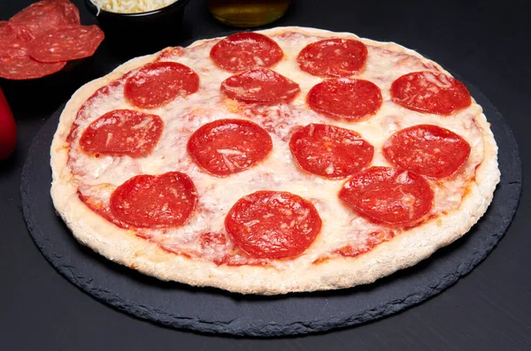 Siyah arka planı olan siyah taştan bir tabakta pepperoni ve mozzarrella peynirli pizza. Dünyanın en ünlü pizzası. Reklamcılık için ideal.