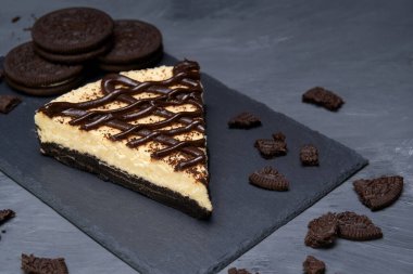 Kurabiye ve kremalı cheesecake süslü taş bir tabakta istiflenmiş kurabiyeler ve gri arka planda kurabiye kırıntıları. Ulusal kurabiye günü veya reklam için kopyalama alanı.