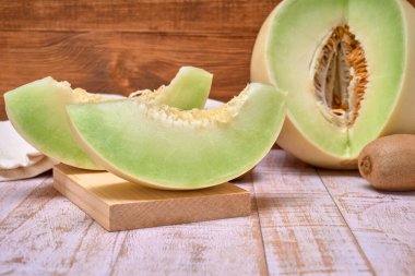 green melon sliced on wooden board with kiwis and a half melon . over a wooden table and wooden background. healthy food concept. Summer fruit clipart