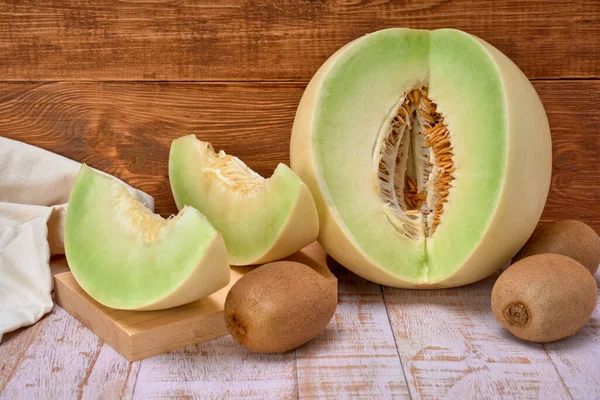 green melon sliced on wooden board with kiwis and a half melon . over a wooden table and wooden background. healthy food concept. Summer fruit