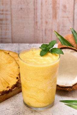Üzerinde nane yaprağı olan ananaslı hindistan cevizli smoothie. Ananas dilimleri ve iki hindistan cevizi. Taş yüzey ve beyaz tahta arka plan. reklam için kopyalama alanı.