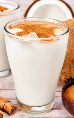 Üzerinde buz ve tarçın tozu olan hindistan cevizi sütü. Beyaz ahşap bir masanın üzerinde tarçın çubukları ve hindistan cevizleri vardı. yakın plan görünümde