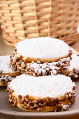 Arjantinli alfajoriler, dulce de leche ve fındık, kahverengi bir tabakta krema şekeri serpiştirilmiş. Bir tarafta bir fincan kahve, ahşap bir masada. Geleneksel bir Arjantin tatlısı. Yakından.