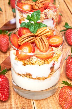 Üzerinde yulaf ezmesi, bal ve nane yaprağı olan fındıklı çilekli parfe. Bir tarafta bütün çilekler ve ahşap bir masada tahta kaşıklar. görünümü kapat