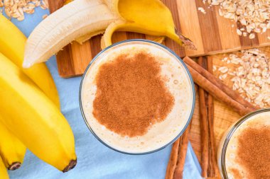 Üzerinde tarçın tozu olan muz ve yulaf püresi, tarçın çubukları, yulaf gevreği, soyulmuş muz, bir demet muz ve mavi peçete. en üstteki görünümde