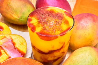 chamoyada or mango smoothie with chamoy and a bamboo straw, a refreshing Mexican drink, served with whole mangoes on a wooden table. clipart