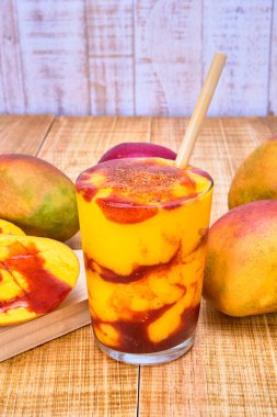 Chamoyada veya mango smoothie ve bambu pipetli, ferahlatıcı bir Meksika içeceği. Ahşap bir masa üzerinde beyaz ahşap bir zemin ile mango ve güveç ile servis edilir.